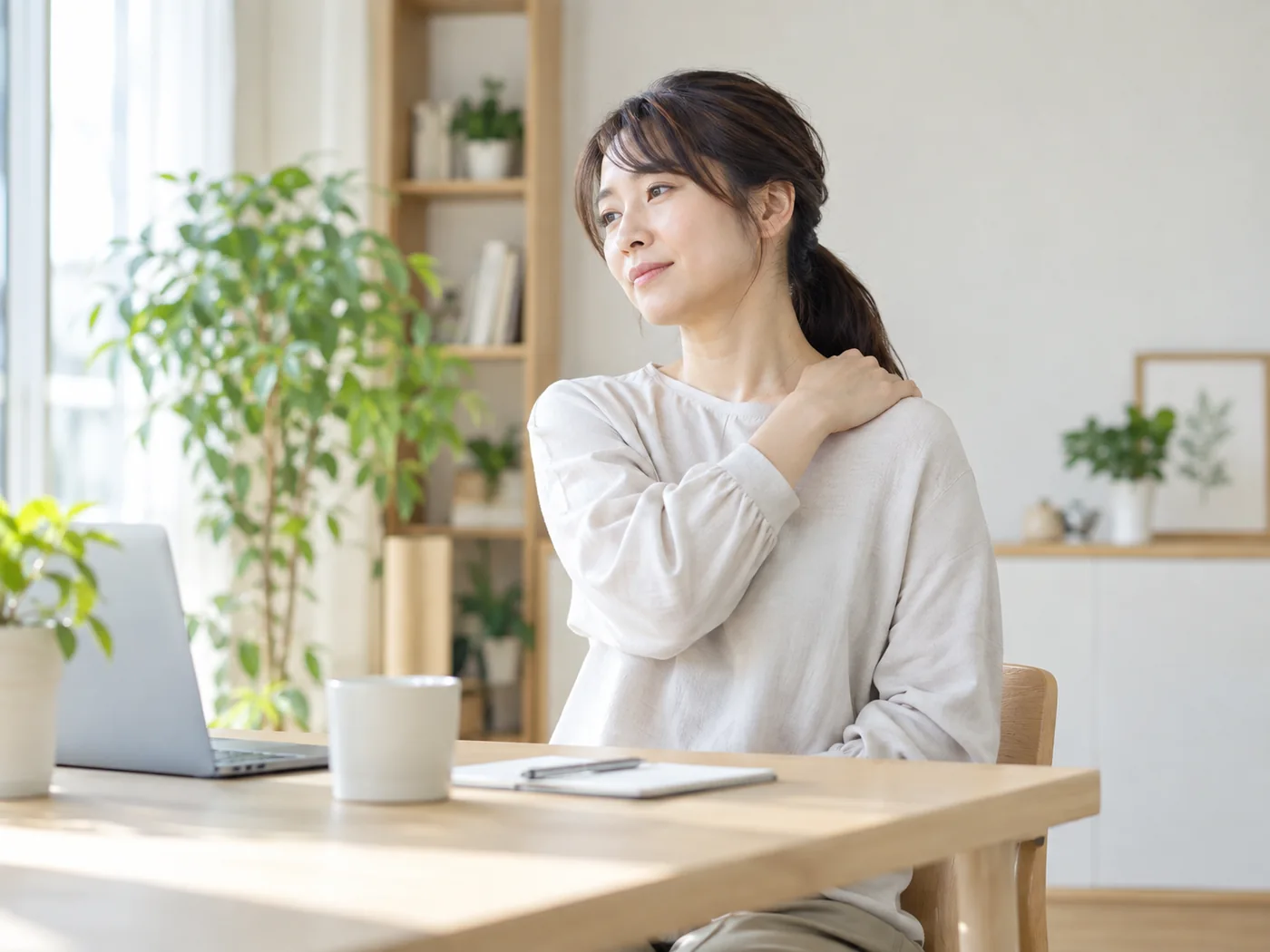 デスクワークの合間に肩へ手を添えて一息つく女性のイメージ