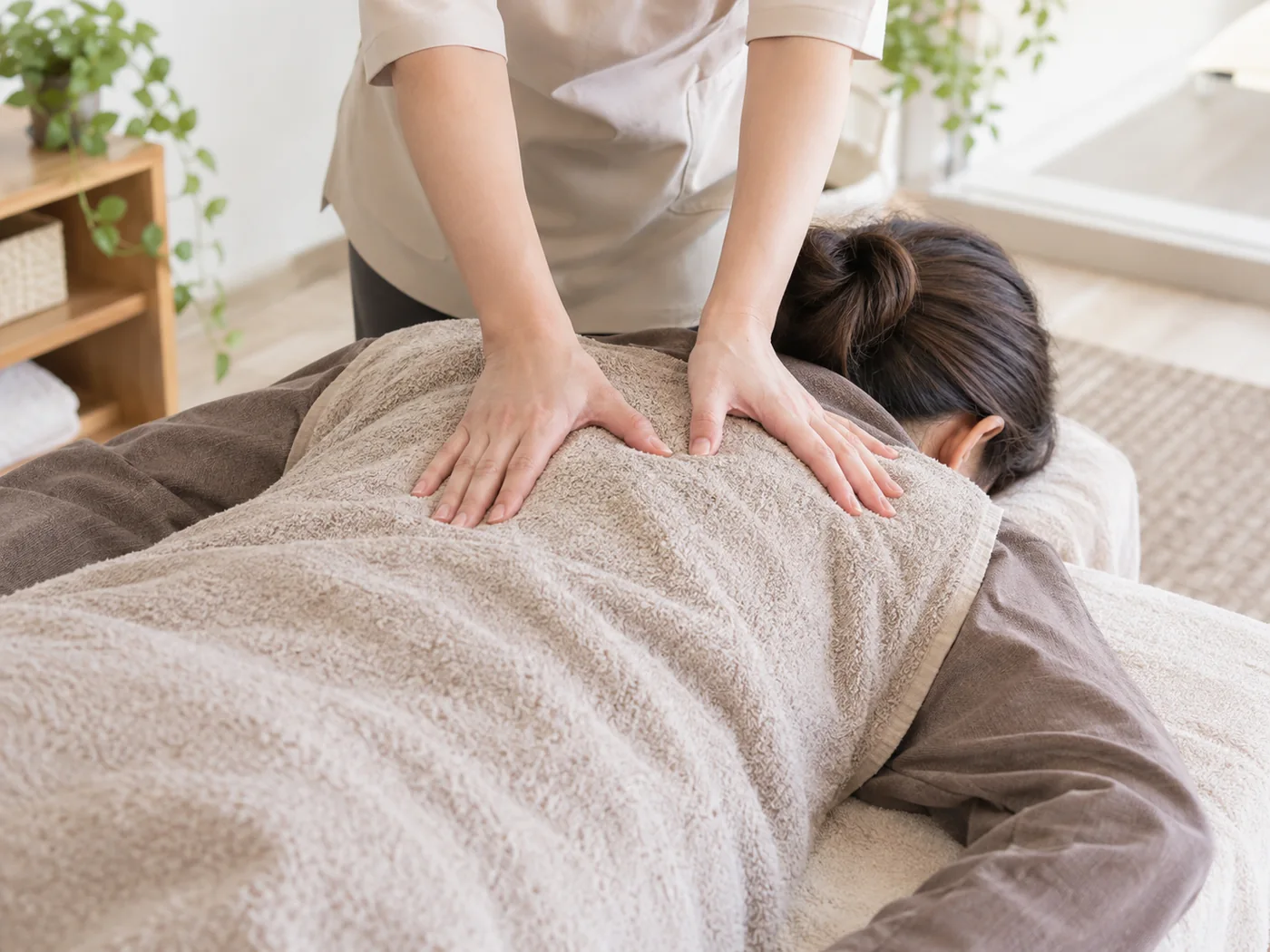着衣の女性の背中をタオル越しに手のひらでケアするイメージ