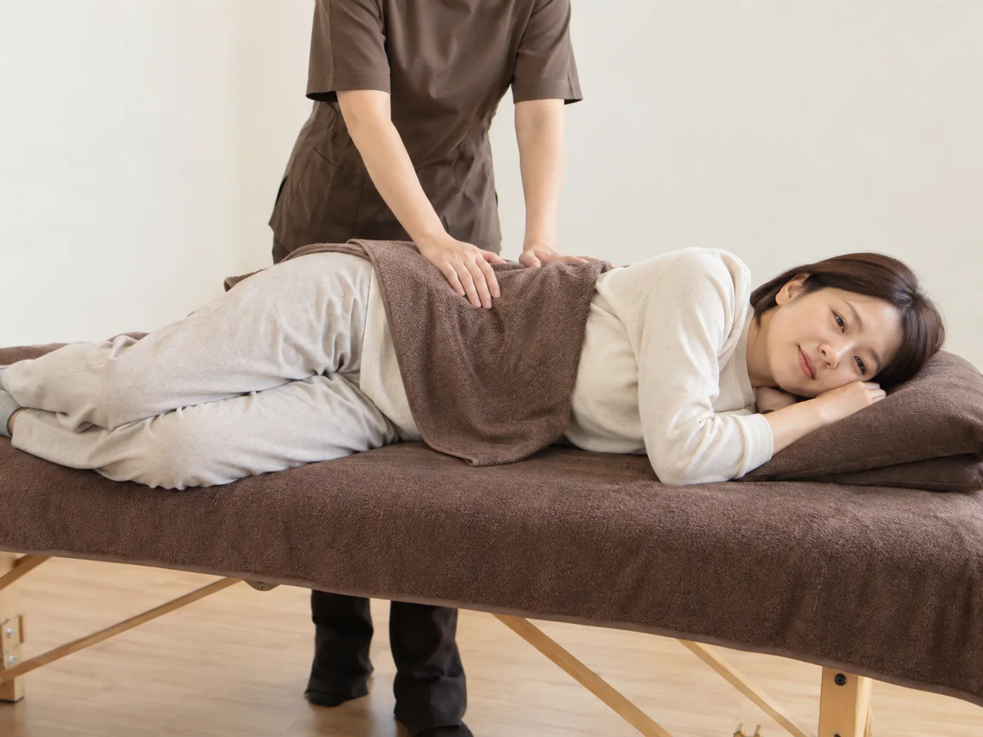 横向きの着衣女性の背中をタオル越しにケアする様子のイメージ